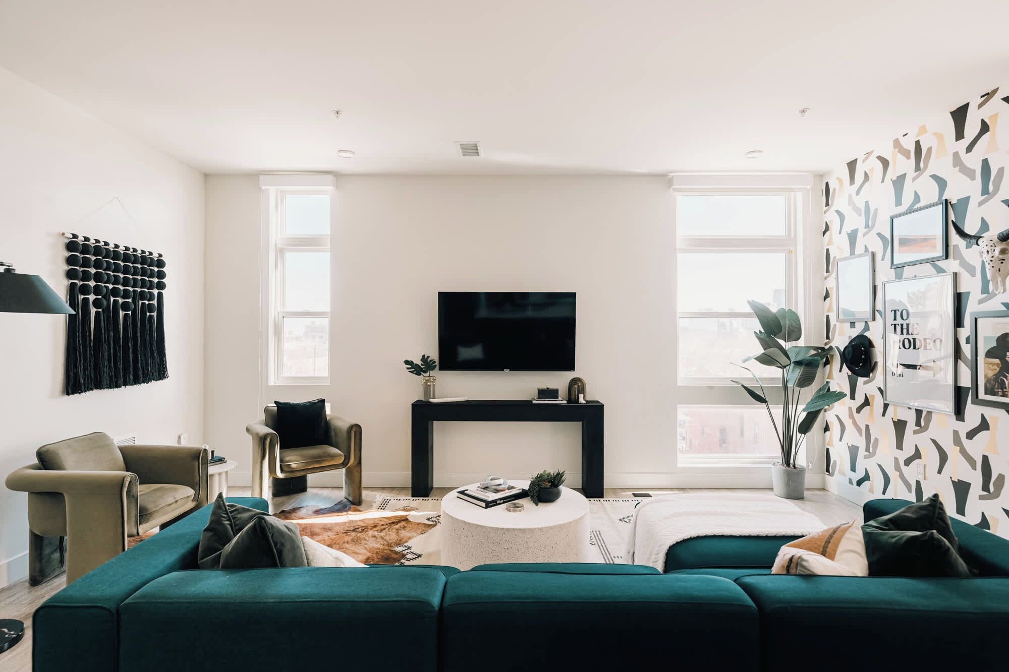 A modern living room with a teal sofa, a black entertainment unit, and a large TV.