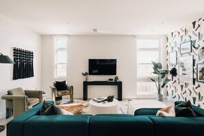 A modern living room with a teal sofa, a black entertainment unit, and a large TV. - Central LoHi Clubhouse | Skyline View | Sleeps 12! (Denver)