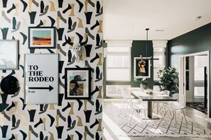 A modern interior with abstract wall art, framed pictures, a dining area with a table and chairs, and a visible door leading outside. - Central LoHi Clubhouse | Skyline View | Sleeps 12! (Denver)