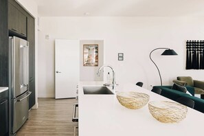A modern kitchen with a white countertop, stainless steel appliances, and a black pendant lamp. - Central LoHi Clubhouse | Skyline View | Sleeps 12! (Denver)