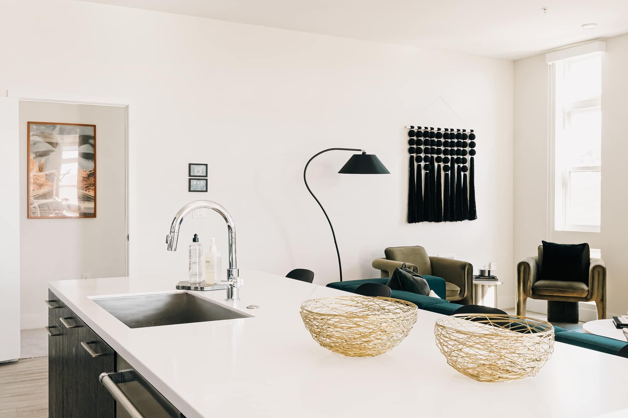 A modern kitchen with a white countertop, stainless steel sink, and a black floor lamp.