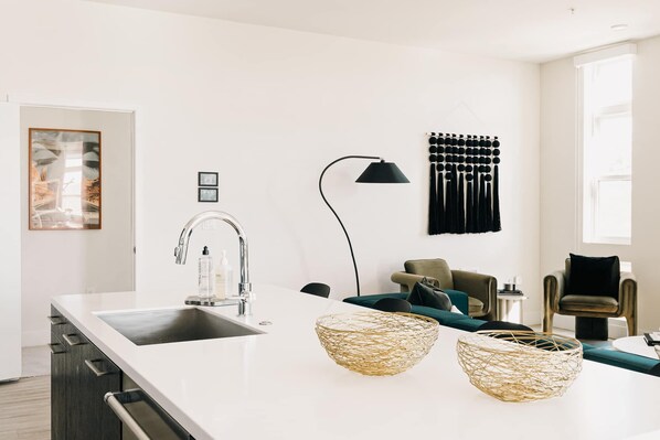 A modern kitchen with a white countertop, stainless steel sink, and a black floor lamp. - Central LoHi Clubhouse | Skyline View | Sleeps 12! (Denver)