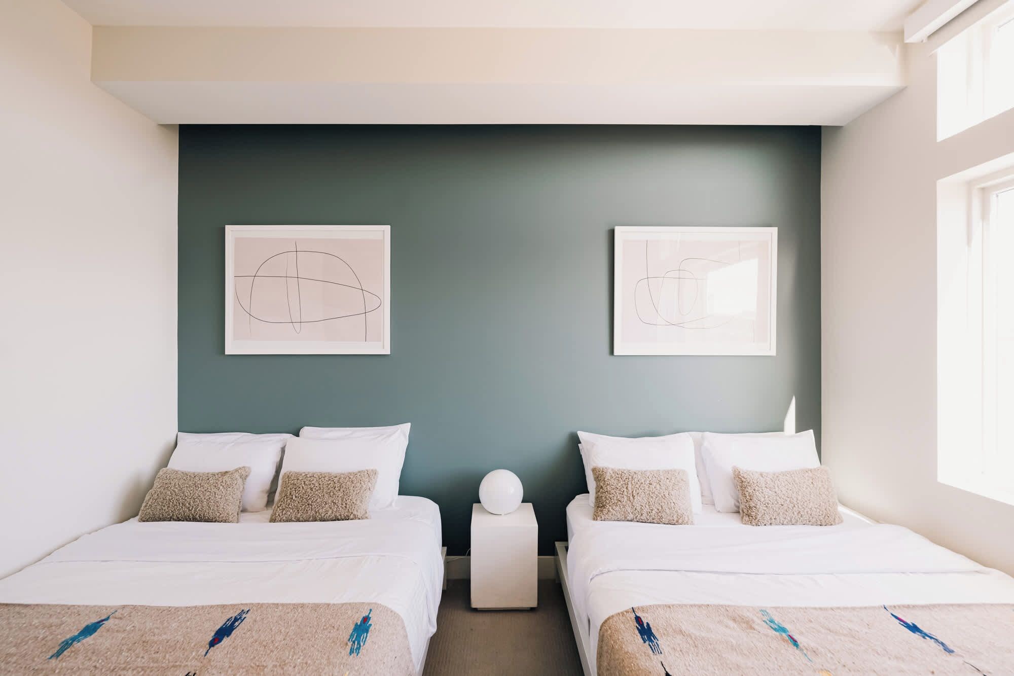 A hotel room with two beds, a dark green accent wall, and two framed abstract artworks.