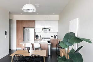 A modern kitchen with a central island, wooden cabinets, stainless steel appliances, and a dining area with a table and chairs. - New Spacious Modern Loft | Center of LoHi (Denver)