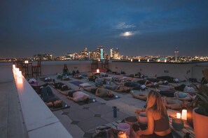A rooftop gathering with people lying on mats, some reading, and a city skyline in the background. - New Spacious Modern Loft | Center of LoHi (Denver)