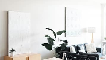 Una sala de estar moderna con comedor, que presenta una mesa blanca, sillas negras, un sofá gris y una planta grande.