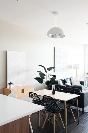 A modern living room with a dining area, featuring a white table, black chairs, a grey sofa, and a large plant. - New Spacious Modern Loft | Center of LoHi (Denver)