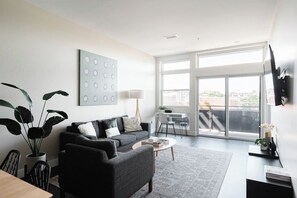 A modern living room with a grey sofa, a coffee table, and a large window offering a view of the city. - New Spacious Modern Loft | Center of LoHi (Denver)