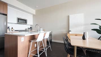 A modern kitchen with a central island, white bar stools, a dining table with black chairs, and a large abstract painting on the wall.