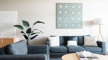 A modern living room with a grey sofa set, a round coffee table, a potted plant, and a wall-mounted artwork.