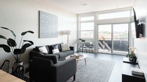 Un salon moderne avec un canapé gris, une table basse et une grande fenêtre donnant sur la ville.