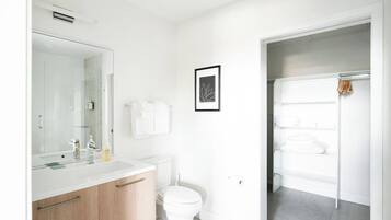 A modern bathroom with a white sink, mirror, and toilet. There is a framed picture on the wall and a towel rack with towels.