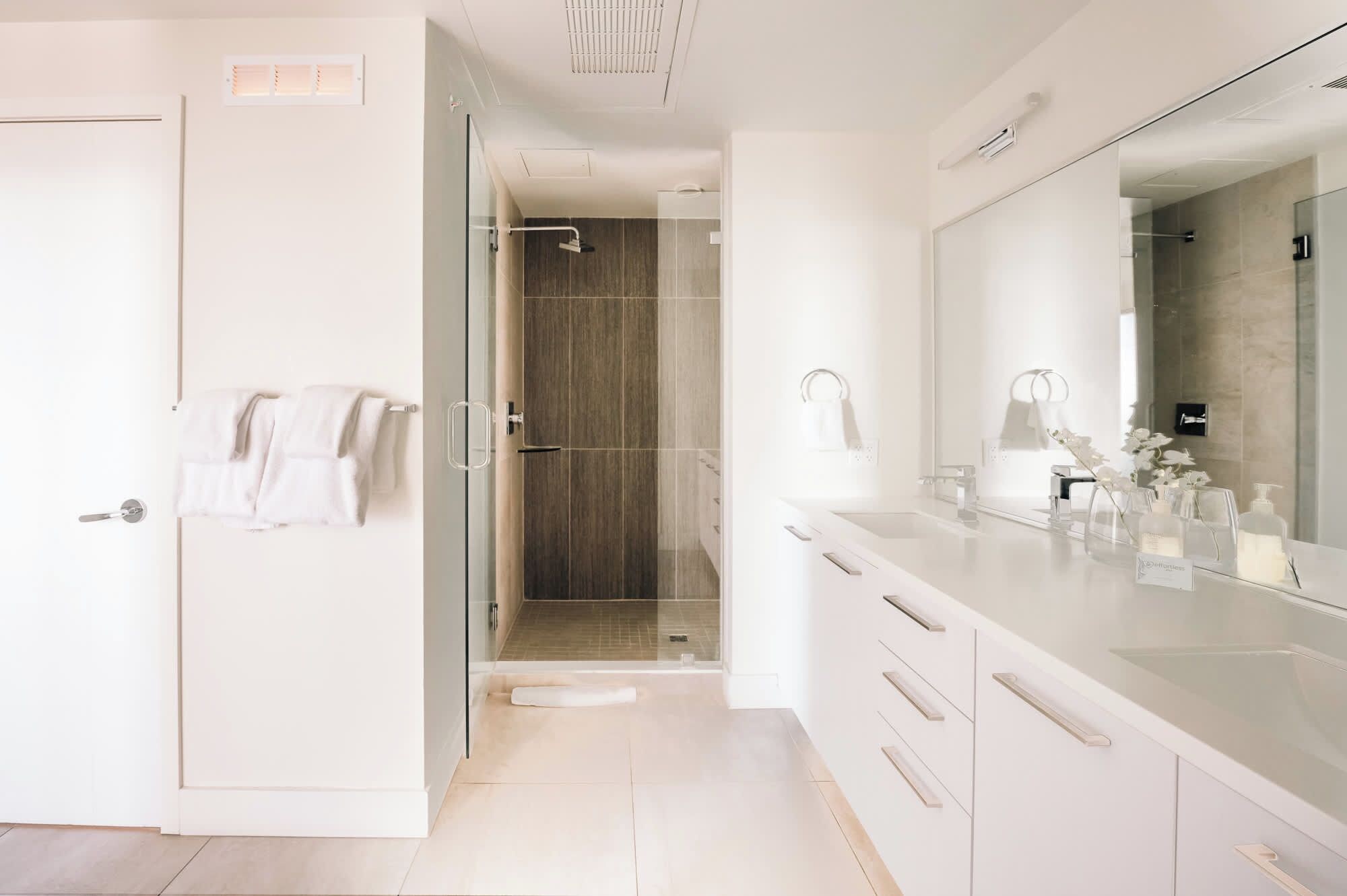 Un baño moderno con cabina de ducha de vidrio, un espejo grande y un tocador con artículos de aseo.