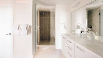 Un baño moderno con cabina de ducha de vidrio, un espejo grande y un tocador con artículos de aseo.