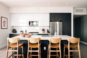 Une cuisine moderne avec des meubles blancs, un réfrigérateur en acier inoxydable, un four à micro-ondes et une cuisinière à gaz.