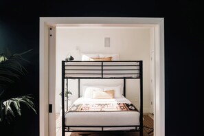 Una cama litera con colchón blanco y manta estampada, una lámpara de noche y una pequeña planta en maceta.