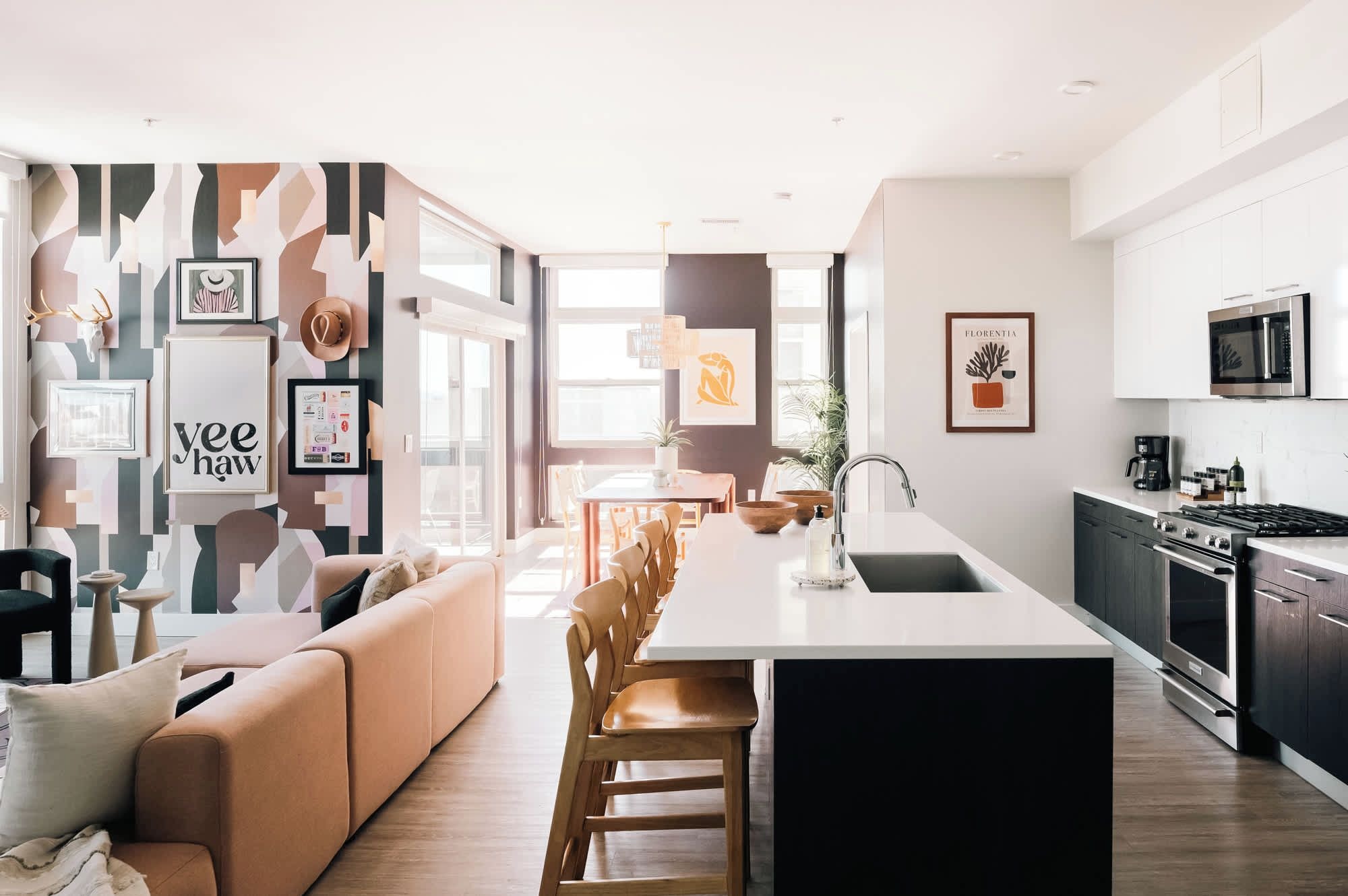Una cocina moderna con una isla central, un área de comedor con sofá y sillas, y una sala de estar con una gran obra de arte en la pared.