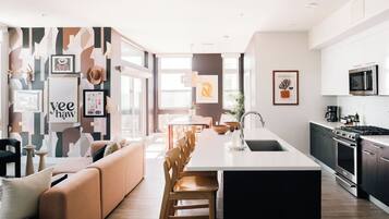 Una cocina moderna con una isla central, un área de comedor con sofá y sillas, y una sala de estar con una gran obra de arte en la pared.
