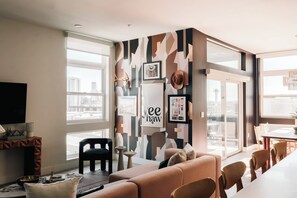 Una sala de estar moderna con un ventanal grande, un sofá, un televisor y una pared decorada con varios objetos enmarcados.