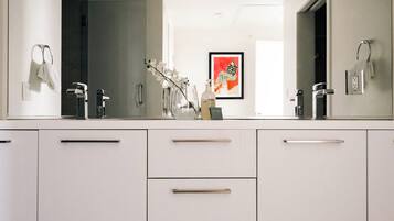Ein modernes Badezimmer mit einem großen Spiegel, weißen Schränken und einem gerahmten Kunstwerk an der Wand.
