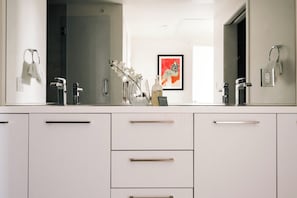 A modern bathroom with a large mirror, white cabinetry, and a framed artwork on the wall. - Skyline Loft | Sweeping City Views | Central LoHi (Denver)