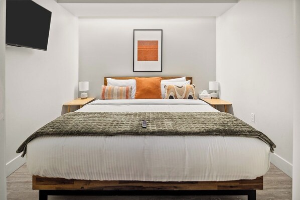 A modern bedroom with a bed, bedside tables, a flat-screen TV, and a framed artwork on the wall.