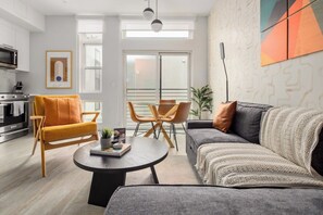 A modern living room with a sofa, armchair, coffee table, and a dining area with chairs.