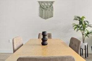 A dining table with a vase, chairs, a macrame wall hanging, and a potted plant.