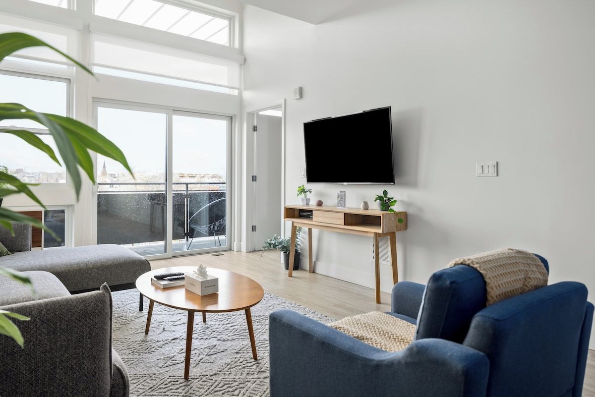 A modern living room with a large window, a flat-screen TV, and comfortable seating.