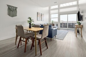 A modern living room with a dining area, large windows, and a view of the city.