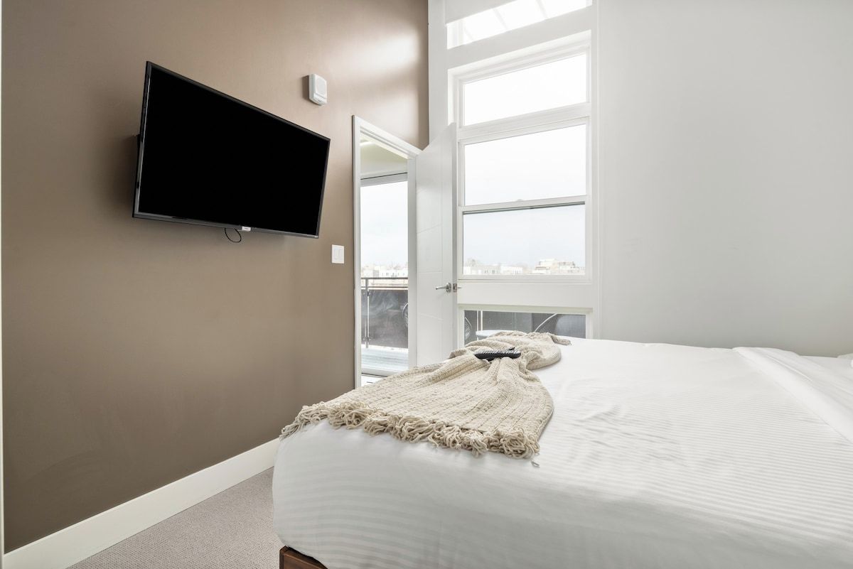 A bedroom with a bed, a television mounted on the wall, and a window with a view.