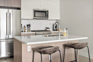 Een moderne keuken met roestvrijstalen apparatuur, een wit aanrecht en twee barkrukken.