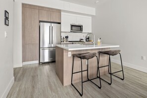A modern kitchen with a stainless steel refrigerator, a microwave, and a sink with bar stools.