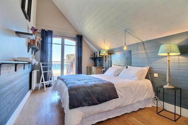 Un dormitorio con una cama grande, un escritorio, una escalera y un ventanal con cortinas.