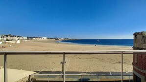 Uitzicht op een strand vanaf een balkon, met een stenen muur en een bakstenen gebouw op de voorgrond.