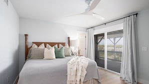 Een slaapkamer met een groot bed, een plafondventilator en uitzicht door een schuifdeur.