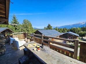Eine Holzterrasse mit Sitzgelegenheit und einem Tisch, gedeckt mit Speisen und Weingläsern.