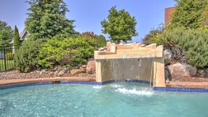 Une piscine agrémentée d’une cascade, entourée de rochers et de verdure.