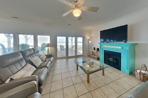 A living room with a sofa, a glass coffee table, a fireplace, a television, and a view of the ocean through large windows. - Sunshiny Daze | Oceanfront in Topsail Beach! (Topsail Beach)