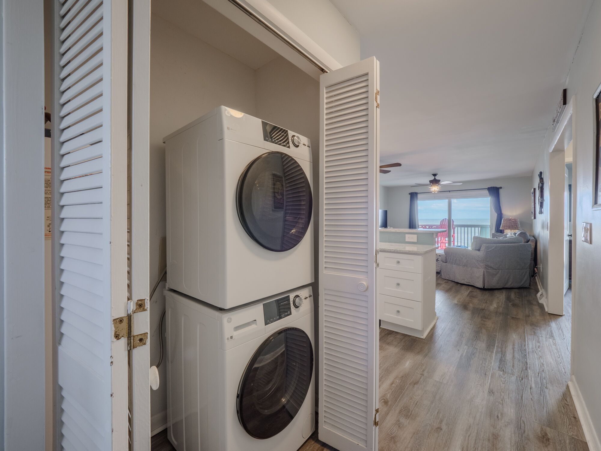 Une buanderie équipée de deux machines à laver et deux sèche-linge superposés, une porte coulissante et une vue sur un balcon avec une chaise rouge.