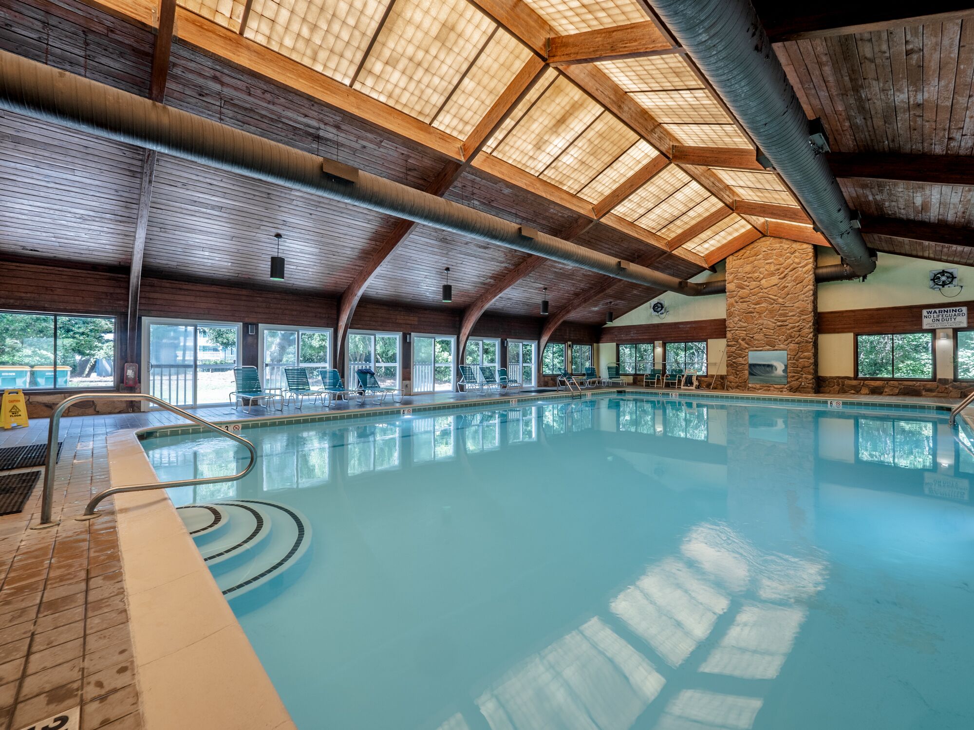 An indoor swimming pool with a high wooden ceiling and large windows.