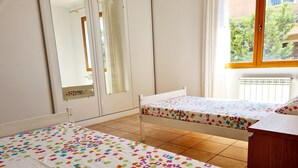 Een slaapkamer met twee bedden, een houten hoofdbord, een raam met gordijnen en uitzicht op groen.
