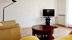Een woonkamer met een bank, een houten tafel, een televisie op een standaard en een vloerlamp.