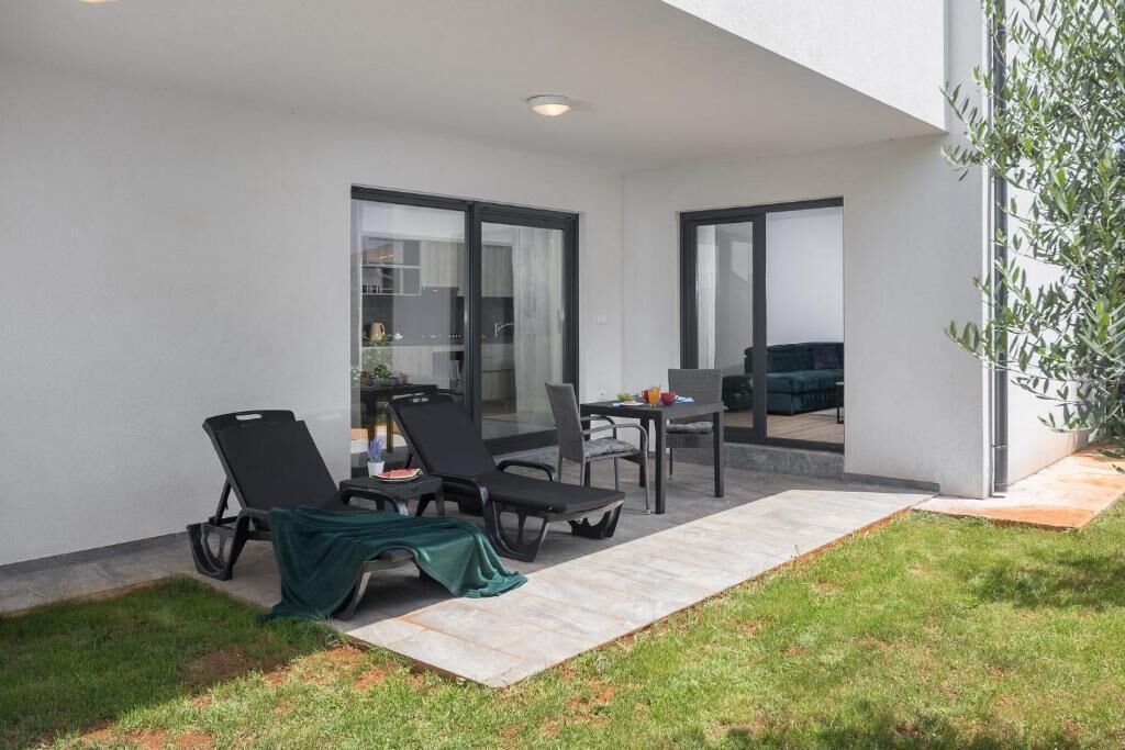 A modern outdoor patio with two lounge chairs, a dining table, and a small garden area.
