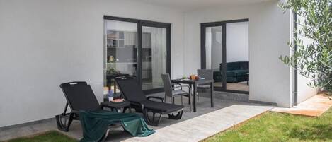 Una moderna veranda esterna con due poltrone relax, un tavolo da pranzo e un piccolo giardino.