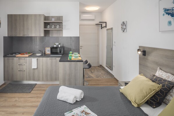 A compact bedroom with a bed, a bedside table, and a small kitchenette area.