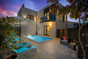 A modern house with a swimming pool, outdoor seating, and a well-lit patio area.