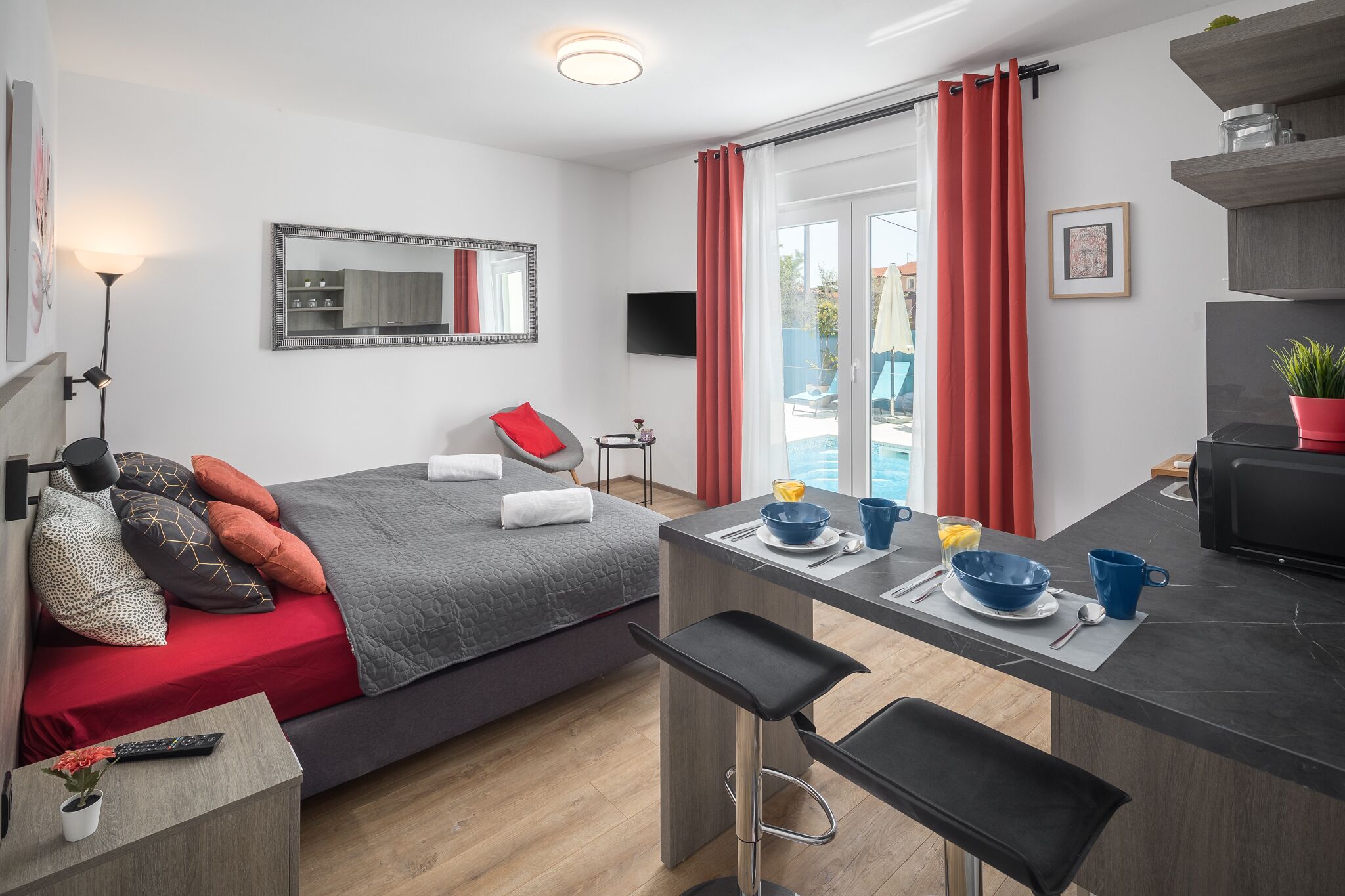 Habitación de hotel moderna con cama, kitchenette pequeña, zona de comedor y puerta corrediza de vidrio al exterior.