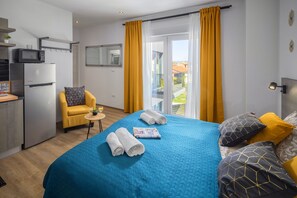 A hotel room with a bed, a chair, a small table, a microwave, and a refrigerator.