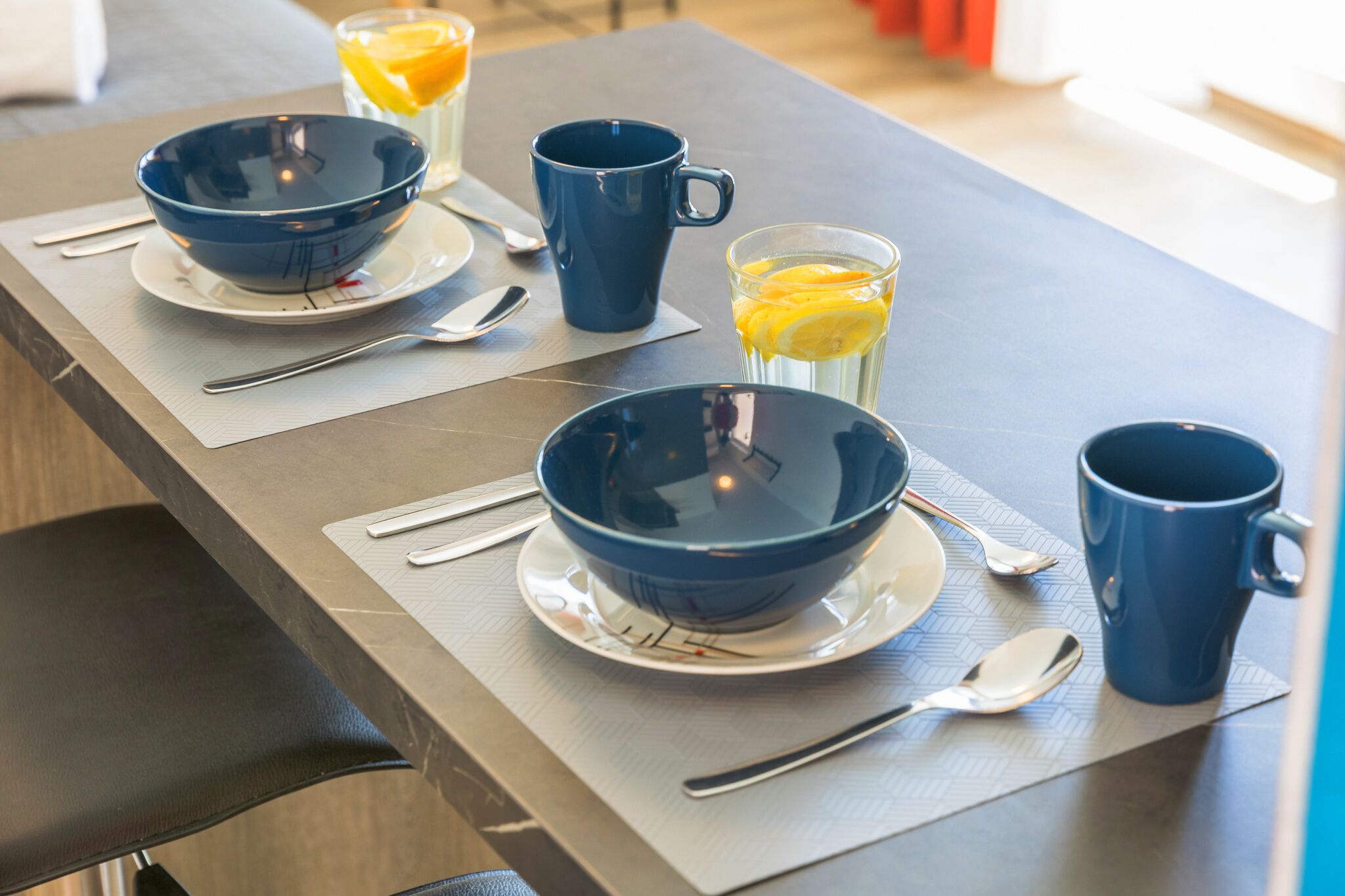 Een ontbijt met twee kommen, twee mokken en een glas sinaasappelsap op een tafel.